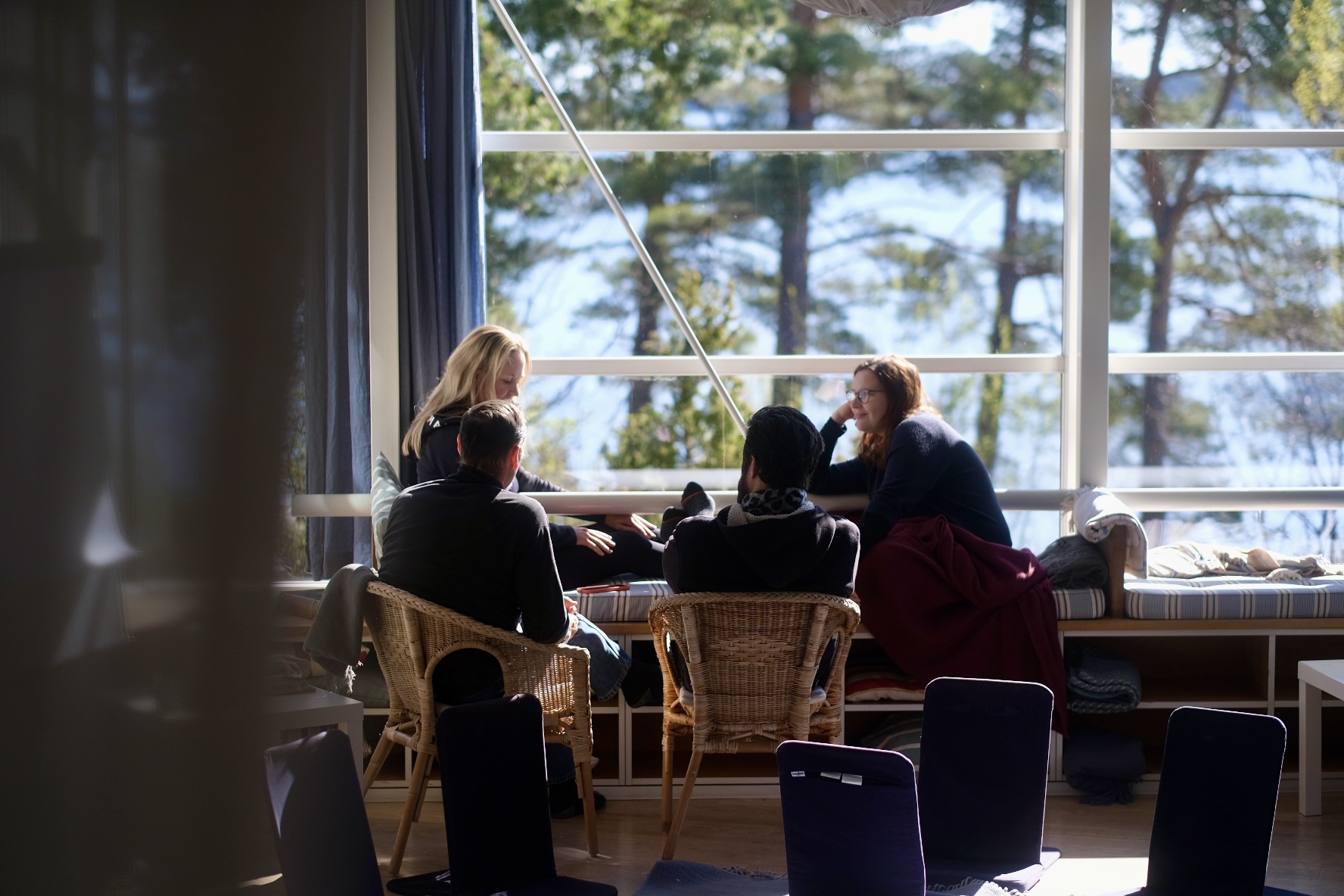 A small group in conversation by a bright window looking out to the pines
