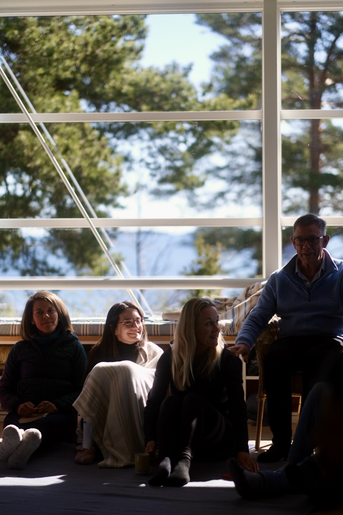 Participants seated together on the floor by tall windows, listening